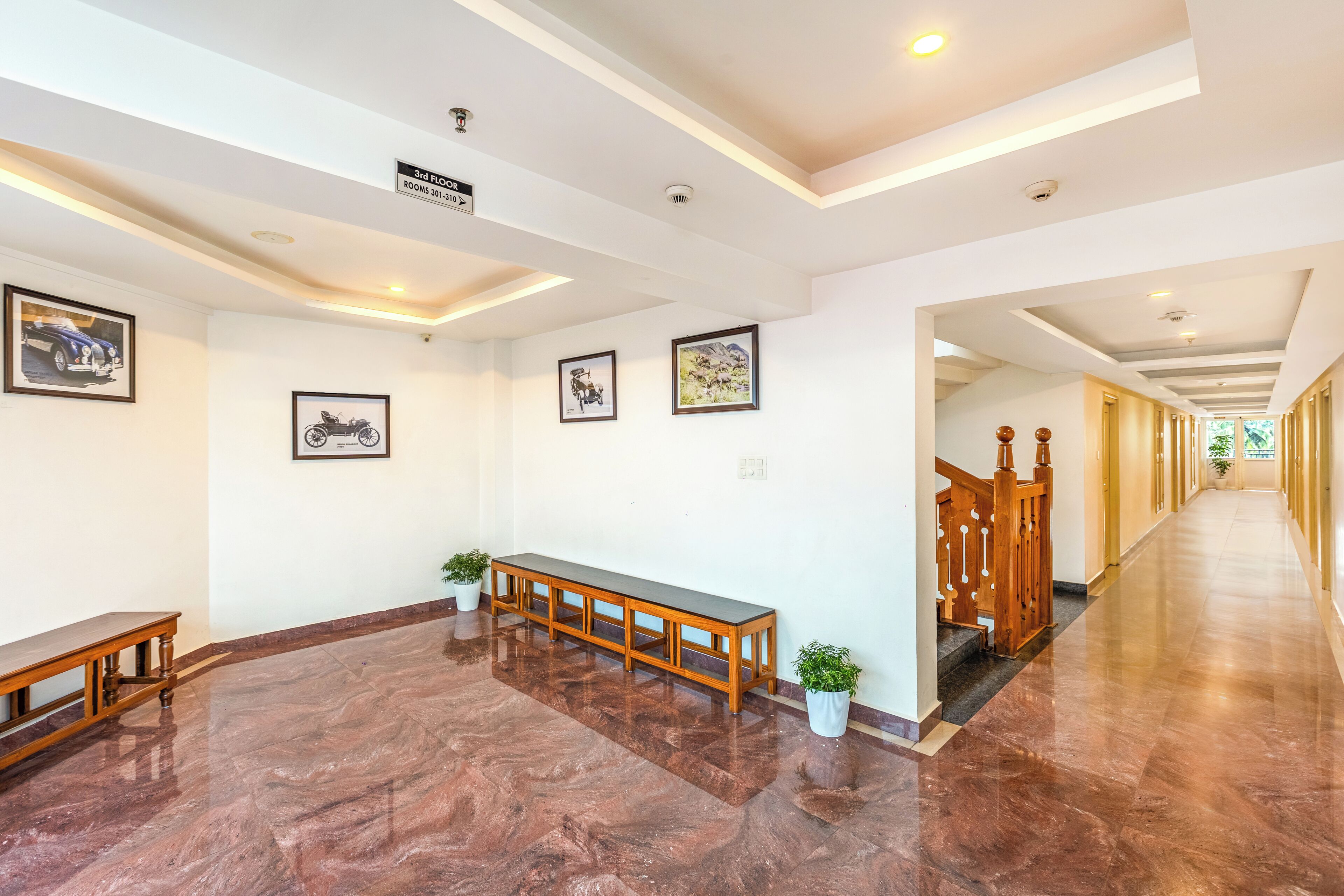 A hotel lobby with a marble floor, wooden benches, framed pictures on the walls, and a staircase leading to another floor.