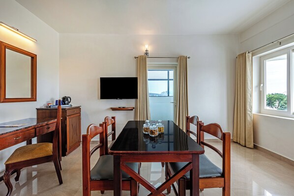 A hotel room with a dining table, chairs, a TV, and a window with curtains. - Sterling Darshan Guruvayur (Guruvayur)