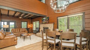 A spacious living room with a fireplace, leather sofa, dining table, and wooden chairs.