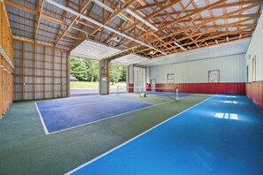 Instalación deportiva cubierta con varias canchas de tenis, pared roja y blanca y estructura de techo de madera.