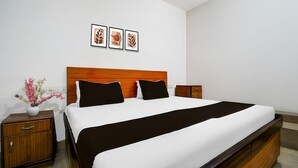 Ein ordentlich eingerichtetes Hotelzimmer mit einem großen Bett, einem hölzernen Nachttisch, einem kleinen Tisch und einem an der Wand befestigten Regal.