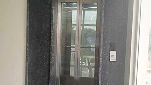 A modern elevator with glass doors, set in a hallway with dark marble walls and a tiled floor.