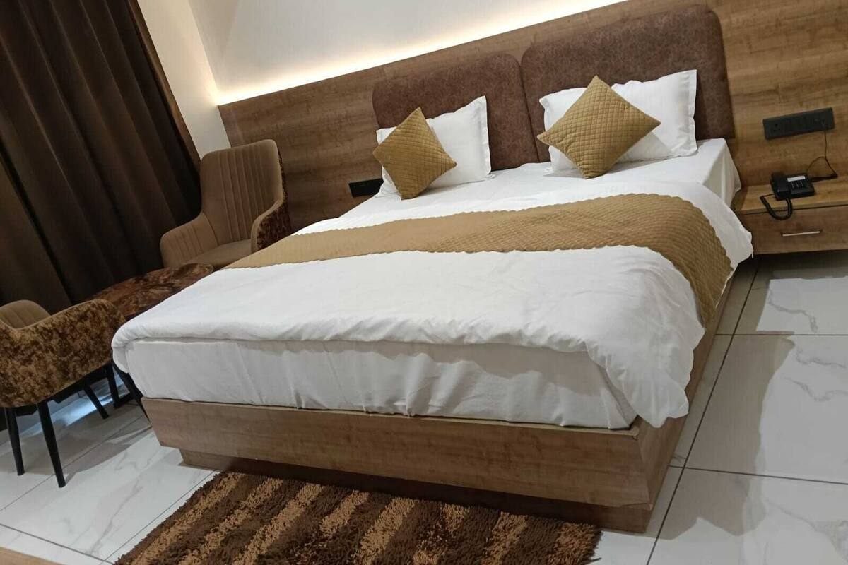 A modern bedroom with a large bed, a wooden headboard, a bedside table with a phone, and a brown chair.