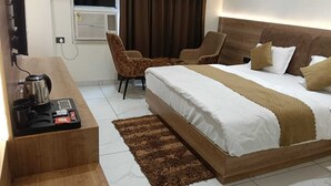 A hotel room with a bed, a desk with a coffee maker, a chair, and a TV.