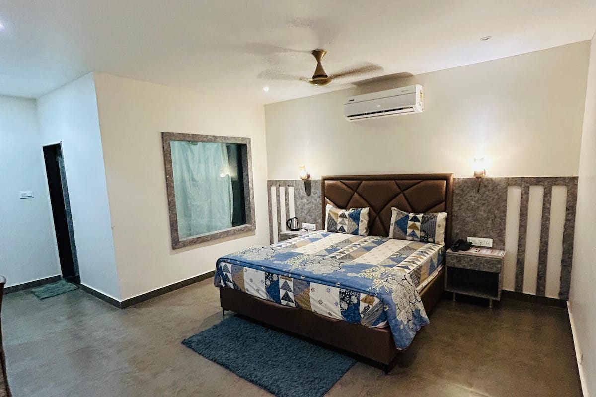 Quarto com cama, mesa de cabeceira, janela, ar condicionado e ventilador de teto.