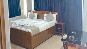 A bedroom with a wooden bed, a nightstand, a desk with a chair, and a ceiling fan. - Paradise Inn (Dehradun)