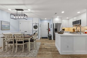 Une cuisine moderne avec des meubles blancs, un îlot central et un coin repas comprenant une table et des chaises.