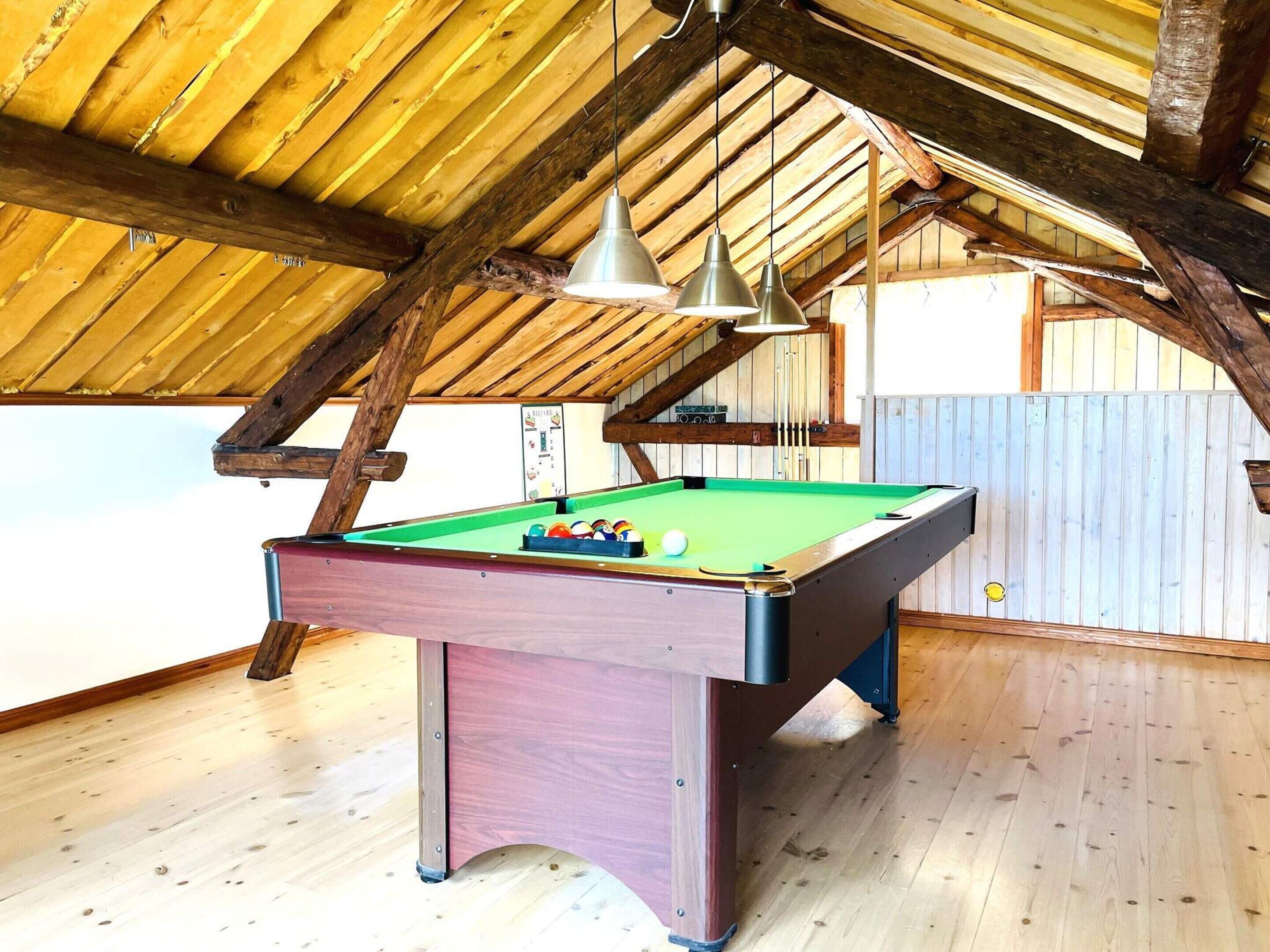 A pool table in a room with wooden beams and a sloped ceiling.