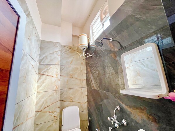 A bathroom with marble tiles, a toilet, a sink with a mirror, and a shower area.