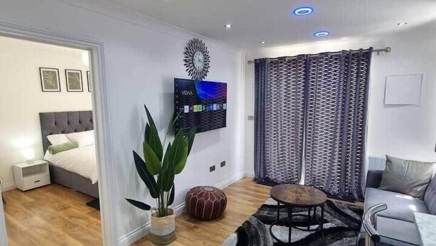 Ein modernes Wohnzimmer mit Flachbildfernseher, einem Essbereich mit Tisch und Stühlen sowie einer gemütlichen Sitzecke mit Sofa und Hocker.