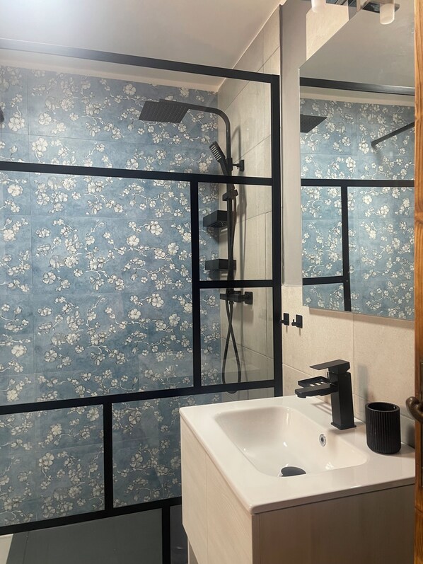 A bathroom with a shower area, a sink, and a mirror.