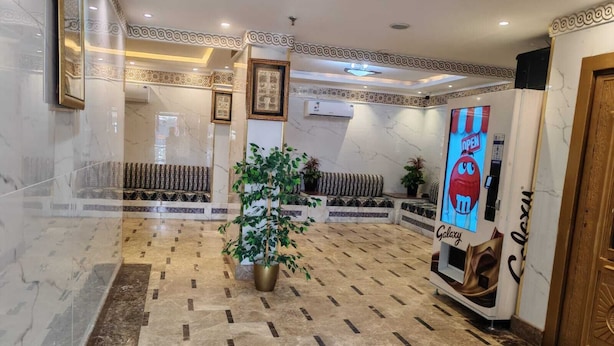 A lobby with marble flooring, a large potted plant, a Galaxy-themed poster, and a patterned bench area. - Manar Al Azhar Hotel (Makkah)