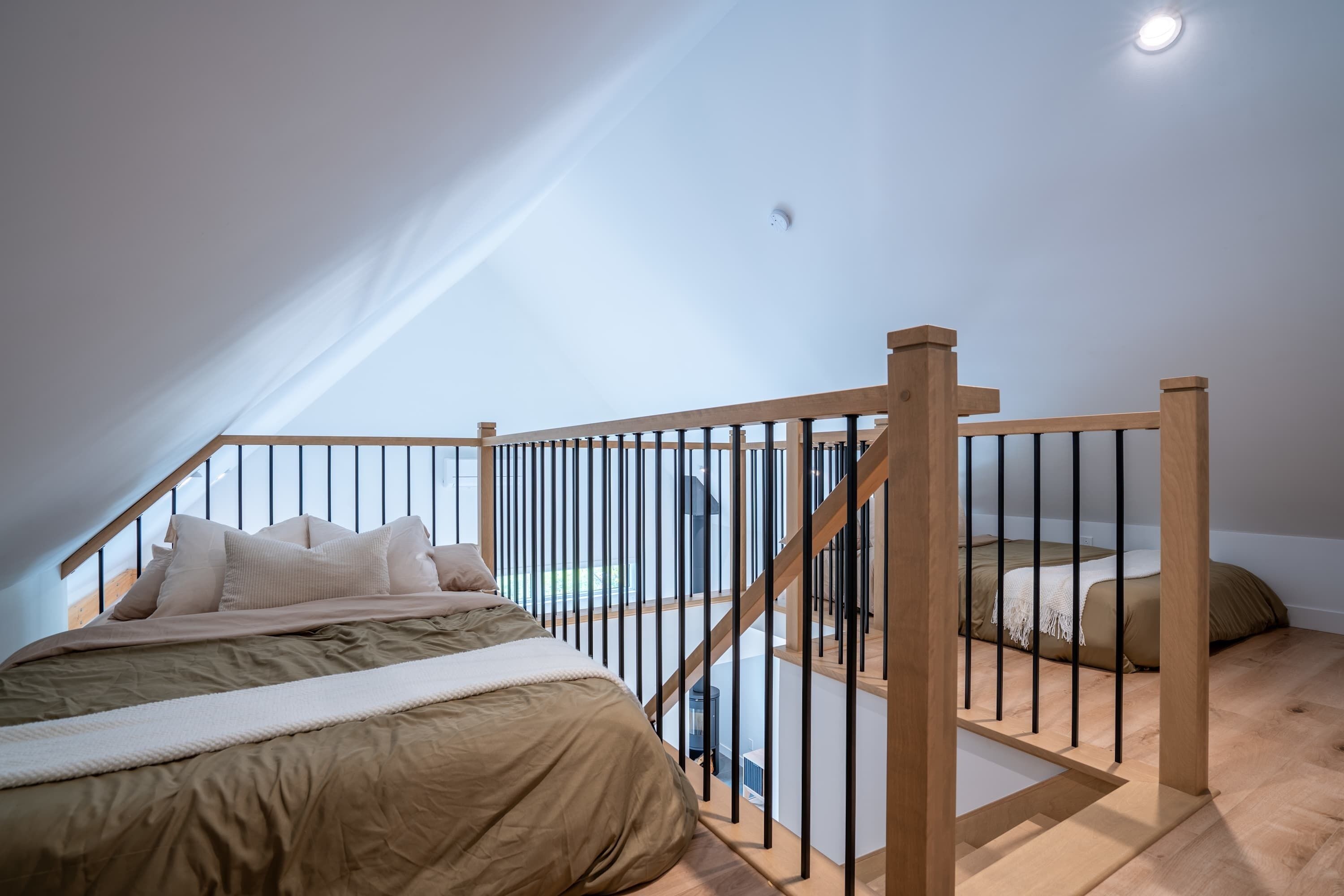 A bedroom with a wooden bed, a view of the outdoors, and a staircase with a railing.