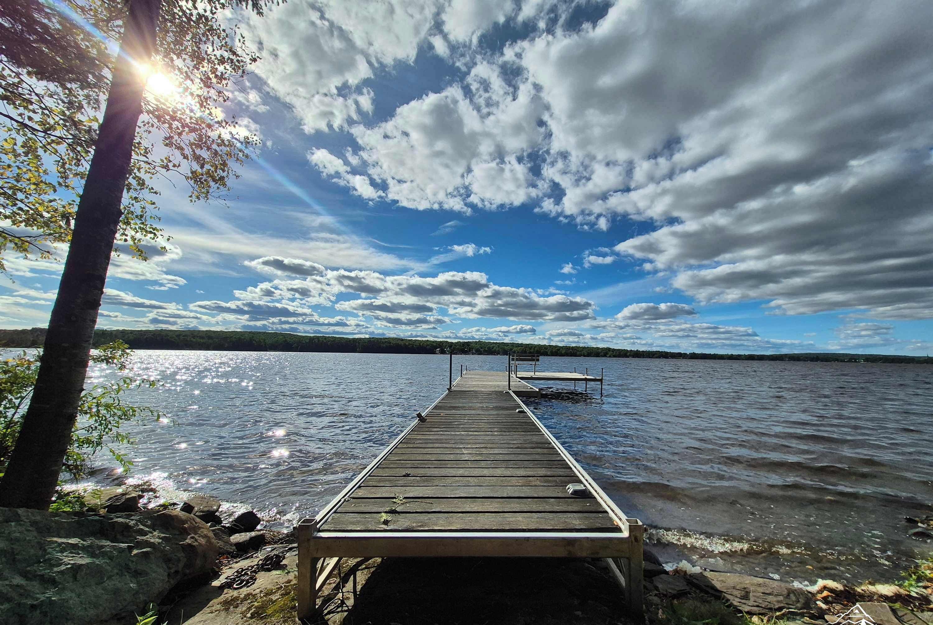 Eine Holzstege ragt in einen See, der bewölktem Himmel entgegenführt.