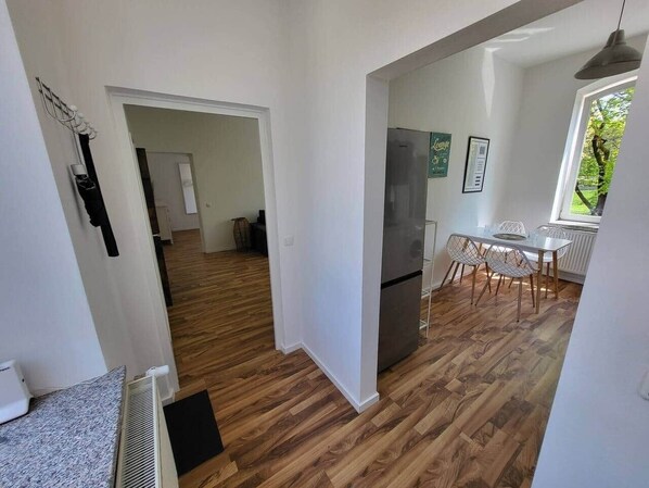 A modern kitchen with a refrigerator, dining table, and chairs. There is a wooden floor and white walls. - To complete (Oberschleißheim)