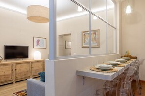 A modern living room with a TV, wooden cabinets, a sofa, and a dining area with clear chairs and a long table. - Sant'Ambrogio Elegant Apartment (Firenze)