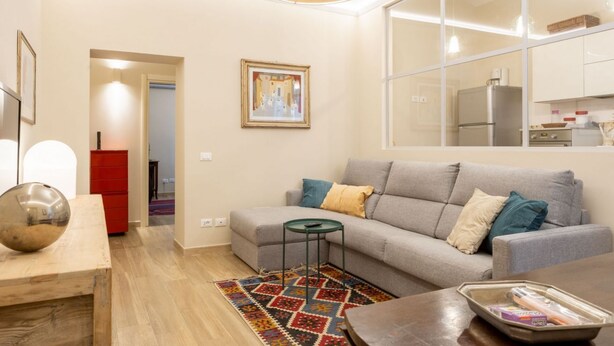 Un salon moderne avec un canapé gris, une petite table ronde et un tapis coloré.