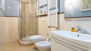 Une salle de bain avec une douche à parois de verre, des toilettes, un bidet et un lavabo équipé de produits de toilette.