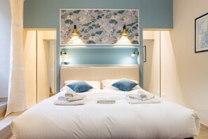 A hotel room with a bed, two bedside lamps, a headboard with floral wallpaper, and a window with curtains. - Sant'Ambrogio Elegant Apartment (Firenze)
