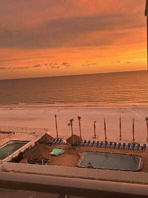 A beach resort with a pool area, lounge chairs, and a view of the ocean at sunset.