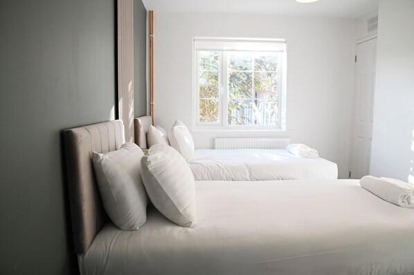 Ein Schlafzimmer mit einem großen Bett, einem kleineren Bett und einem Fenster mit Blick auf Grünflächen.