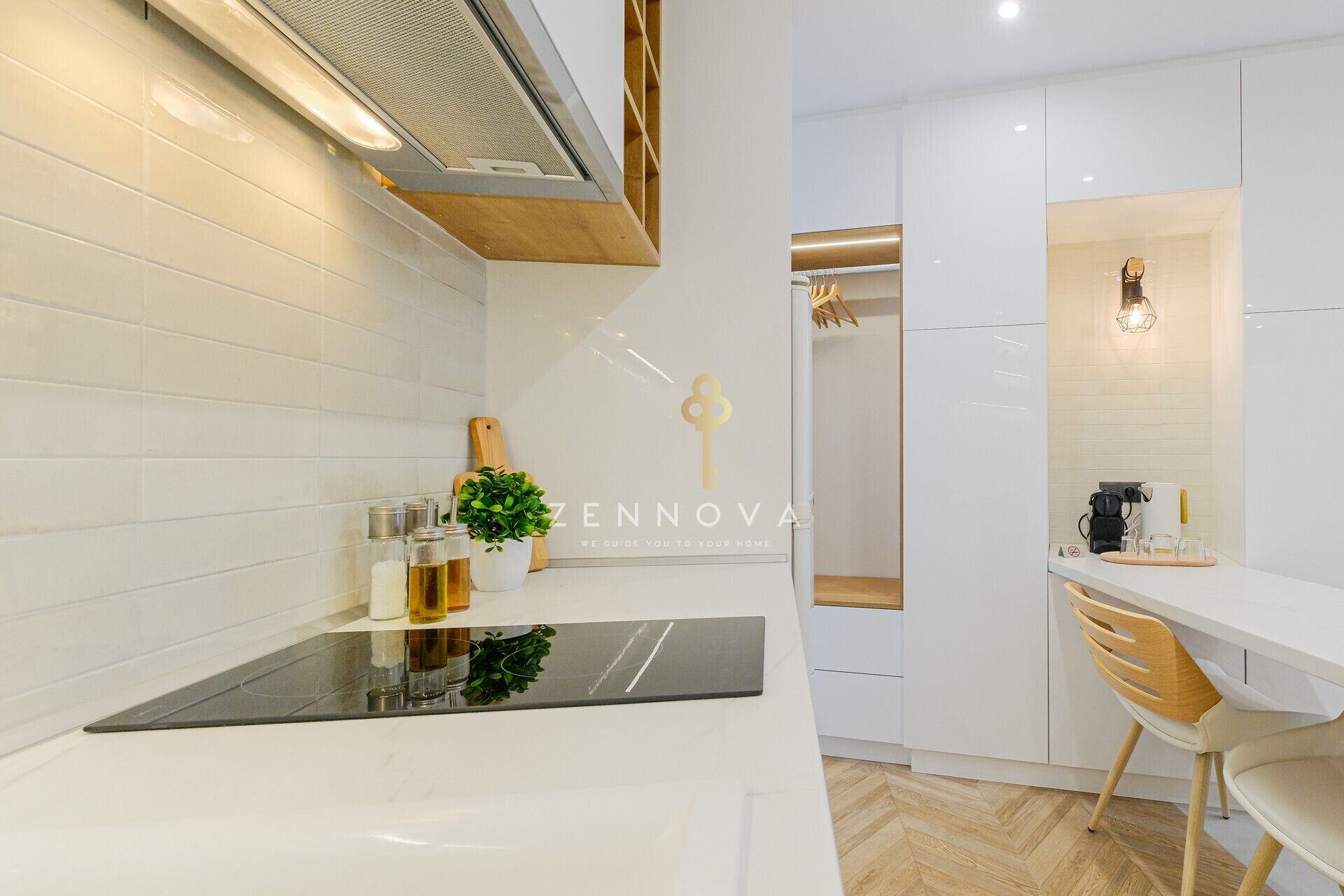 A modern kitchen with white cabinetry, a black countertop, and a wooden chair. There is a plant on the counter and a coffee maker on the right.