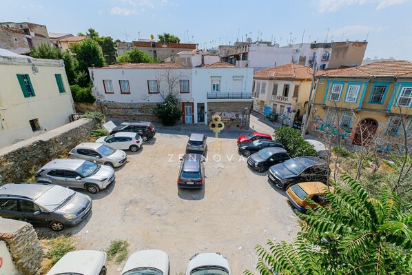 A parking lot with several cars, surrounded by buildings with various architectural styles, including a white building with green shutters and a yellow building with blue trim. - Zennova 72 Tsinari Luxury Suite (Thessaloniki)