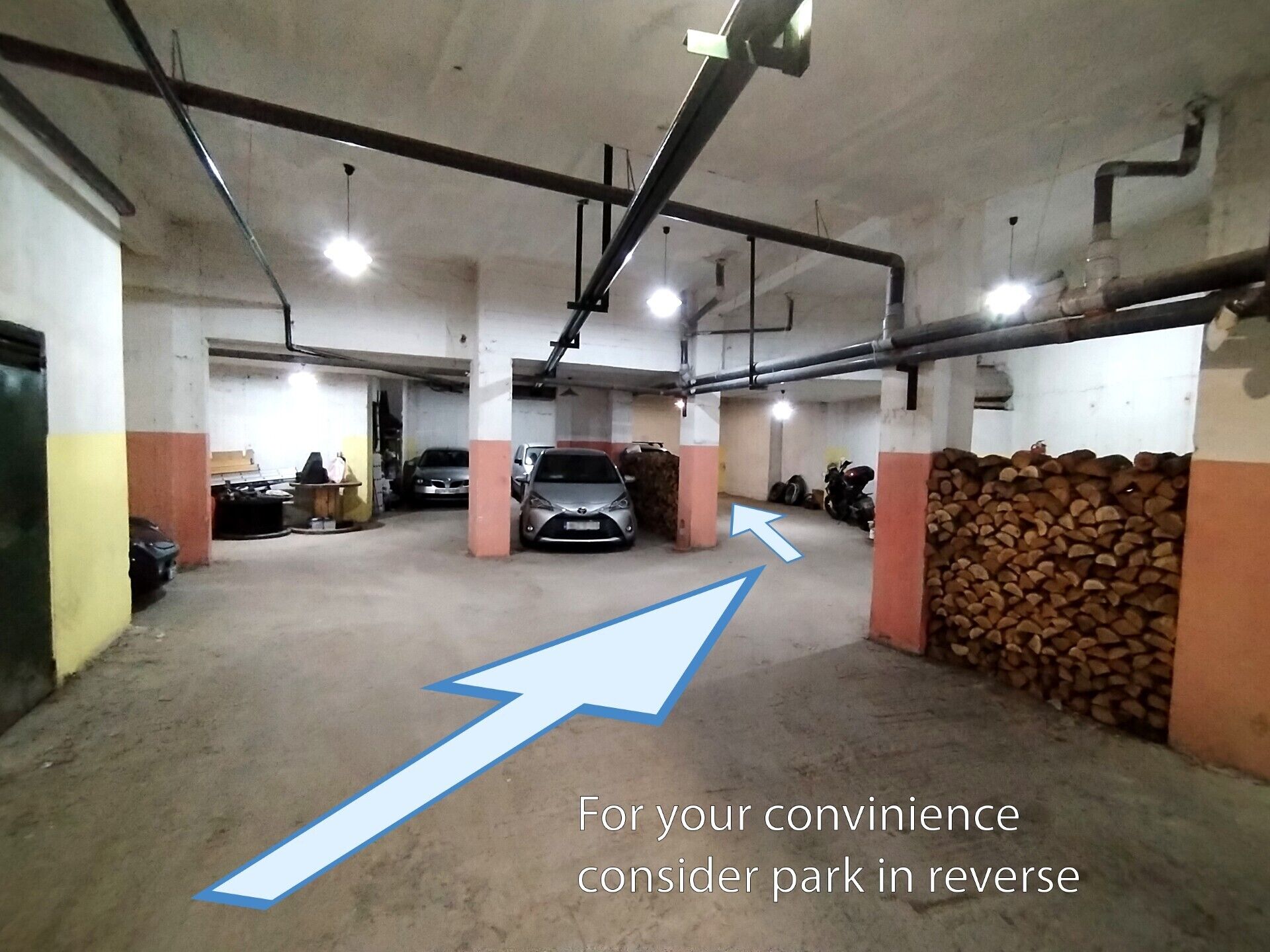 A parking garage with concrete pillars, a car, and a stack of logs.