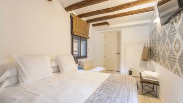 Un dormitorio con cama, vigas de madera, ventana con persiana, puerta y pared con estampado.