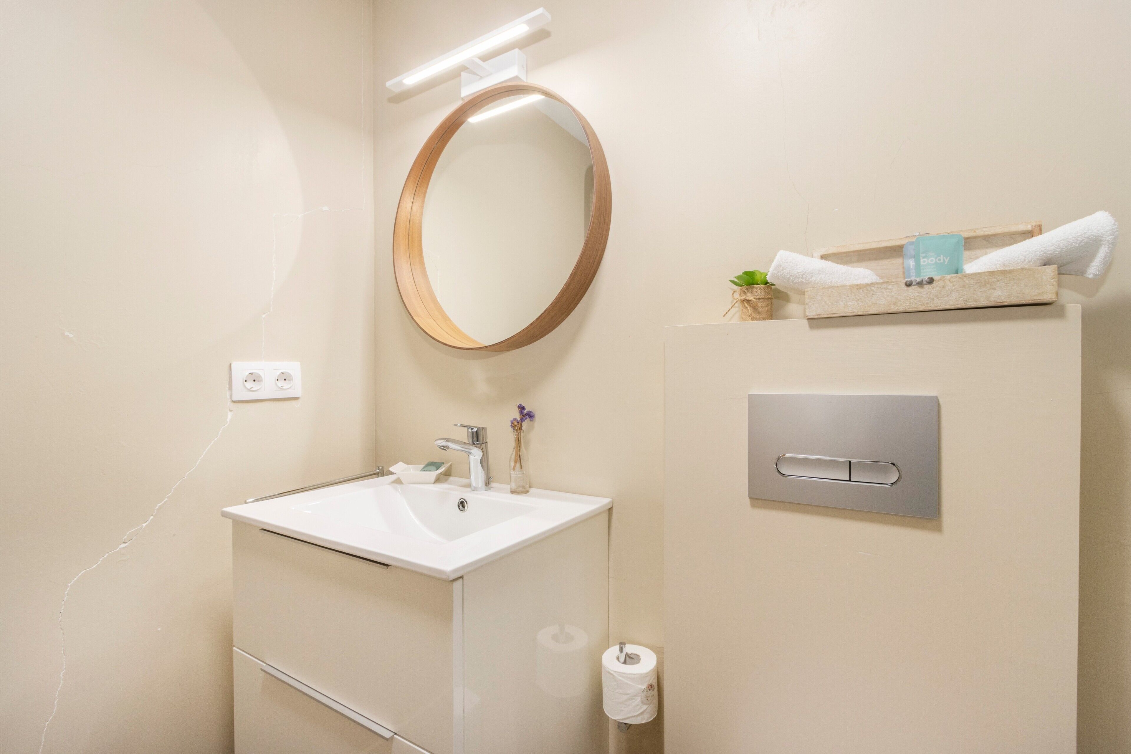 Et badeværelse med hvid vask, spejl, håndklædetørrestativ og toiletpapirholder.