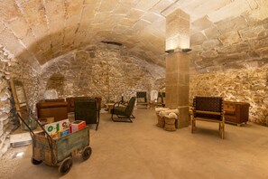 Una habitación de paredes de piedra con un carro de madera, asientos acolchados y una chimenea.