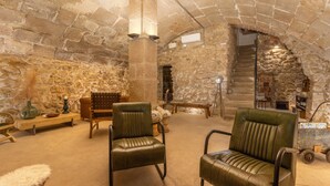 Habitació de parets de pedra amb cadires de cuir, una banca de fusta i una taula petita amb un vas.