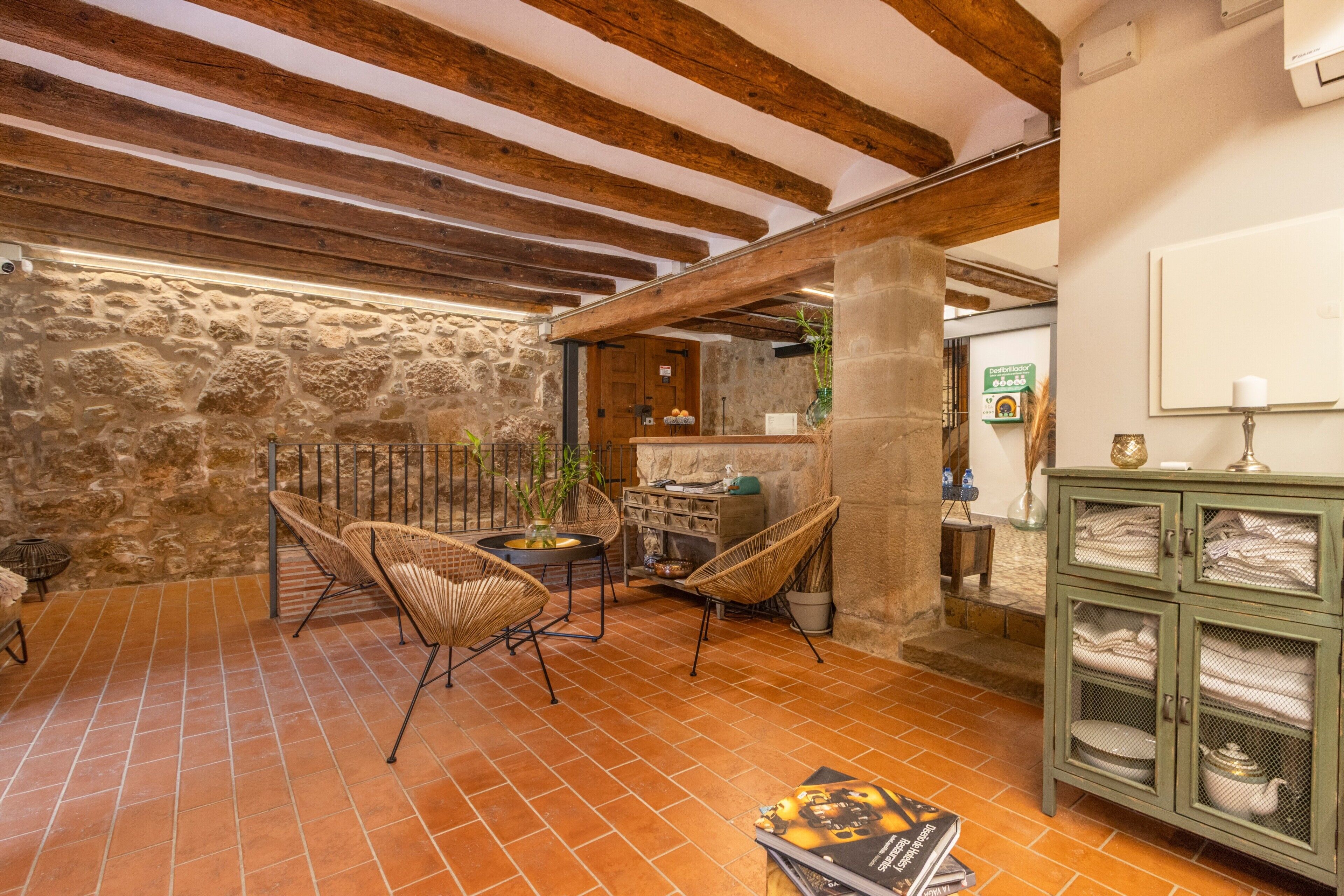 A rustic interior with exposed wooden beams, stone walls, wicker chairs, a tiled floor, and a cabinet with glass doors.