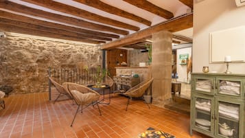 A rustic interior with exposed wooden beams, stone walls, wicker chairs, a tiled floor, and a cabinet with glass doors.
