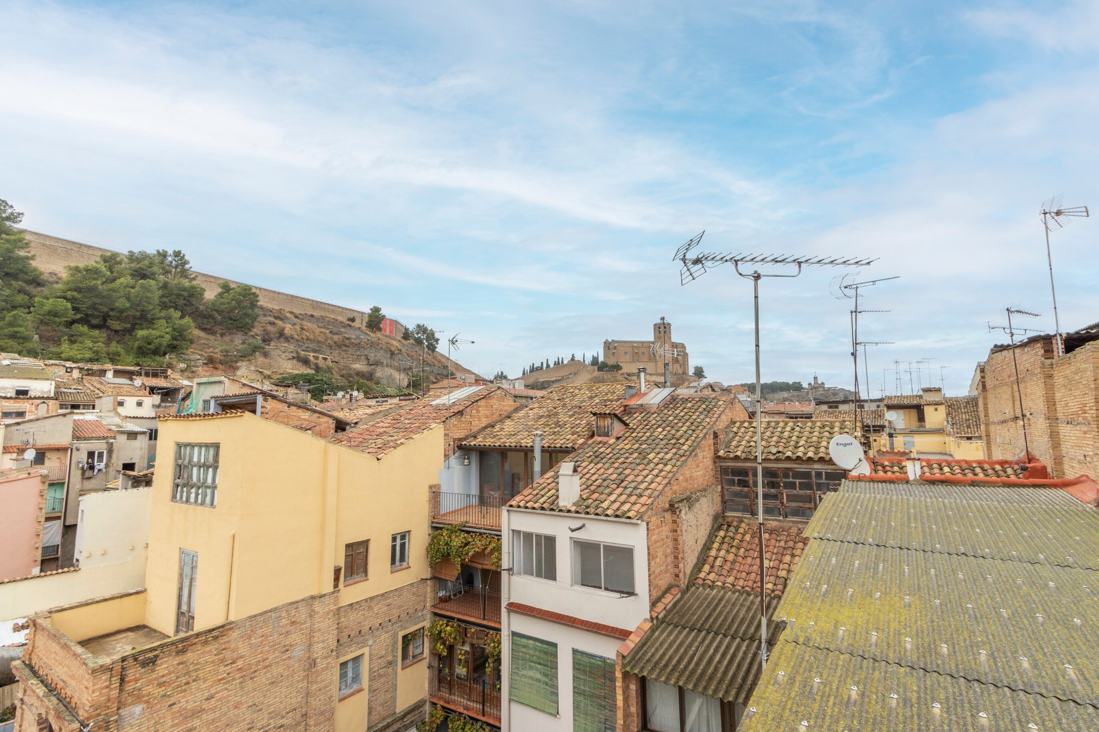 Un quartier résidentiel aux toits recouverts de tuiles en terre cuite, une colline plantée d’arbres et un immeuble doté d’une antenne parabolique.