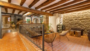 Un interior espaiós amb bigues de fusta al descobert, una paret de pedra i un paviment de rajoles.