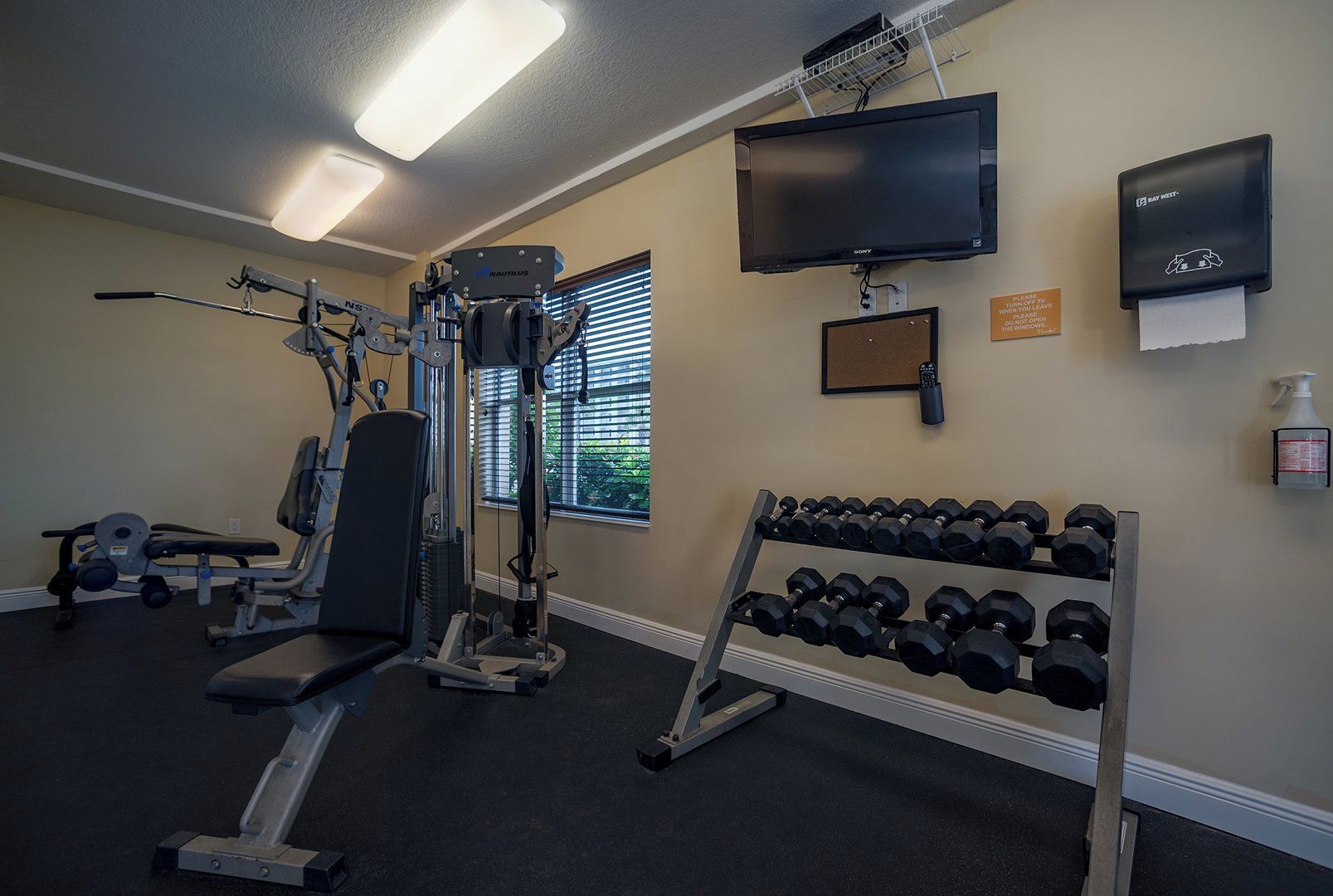 A gym with exercise equipment, a TV, and a wall-mounted hand sanitizer dispenser.