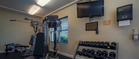 A gym with exercise equipment, a TV, and a wall-mounted hand sanitizer dispenser.