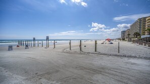 Een strand met een snelheidsbeperkingsbord, een uitkijktoren van de badmeester en een rode tent in het zand.