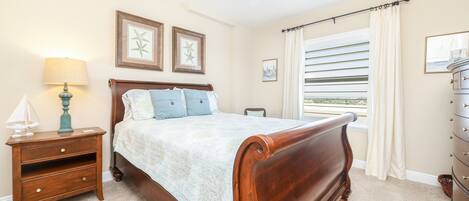 A bedroom with a wooden bed, a nightstand, a lamp, and a dresser.