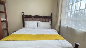 Een bed met een houten hoofdbord, witte beddengoed en een geel accent.