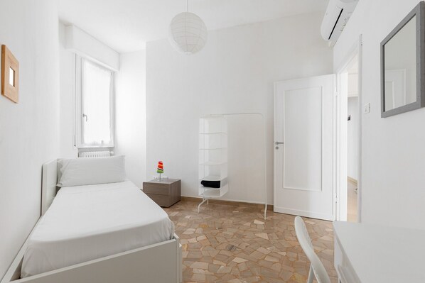 Un dormitorio minimalista con cama, mesita de noche, radiador, lámpara colgante y una puerta.
