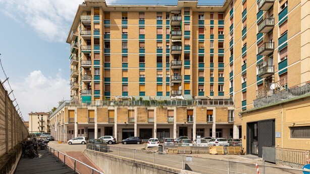 Un edificio residencial de varios pisos con balcones, un estacionamiento al frente y un cielo despejado.