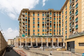 Un edificio residencial de varios pisos con balcones, un estacionamiento al frente y un cielo despejado.