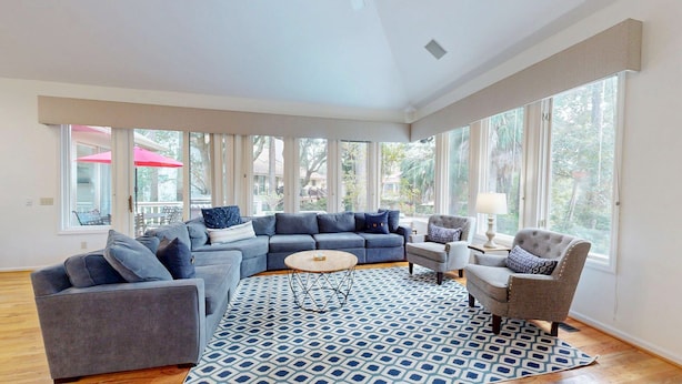 A spacious living room with a sectional sofa, two armchairs, a coffee table, and a patterned rug. Large windows provide ample natural light and views of the outdoors. - 5 Bedroom Near Ocean Home (Hilton Head)