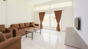 Un salón amplio con un conjunto de sofás, una mesa de centro y un televisor de pantalla plana montado en la pared.