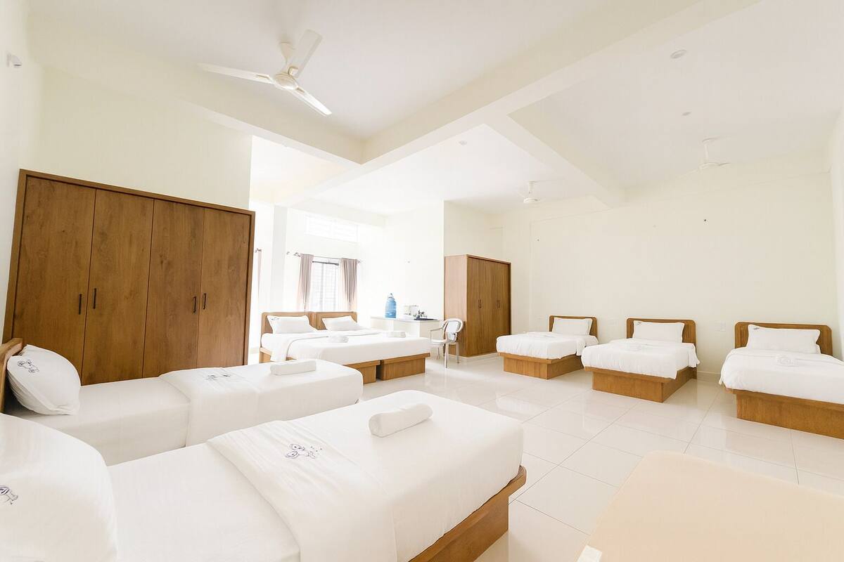 A hotel room with four single beds, wooden wardrobes, a desk, and a chair.