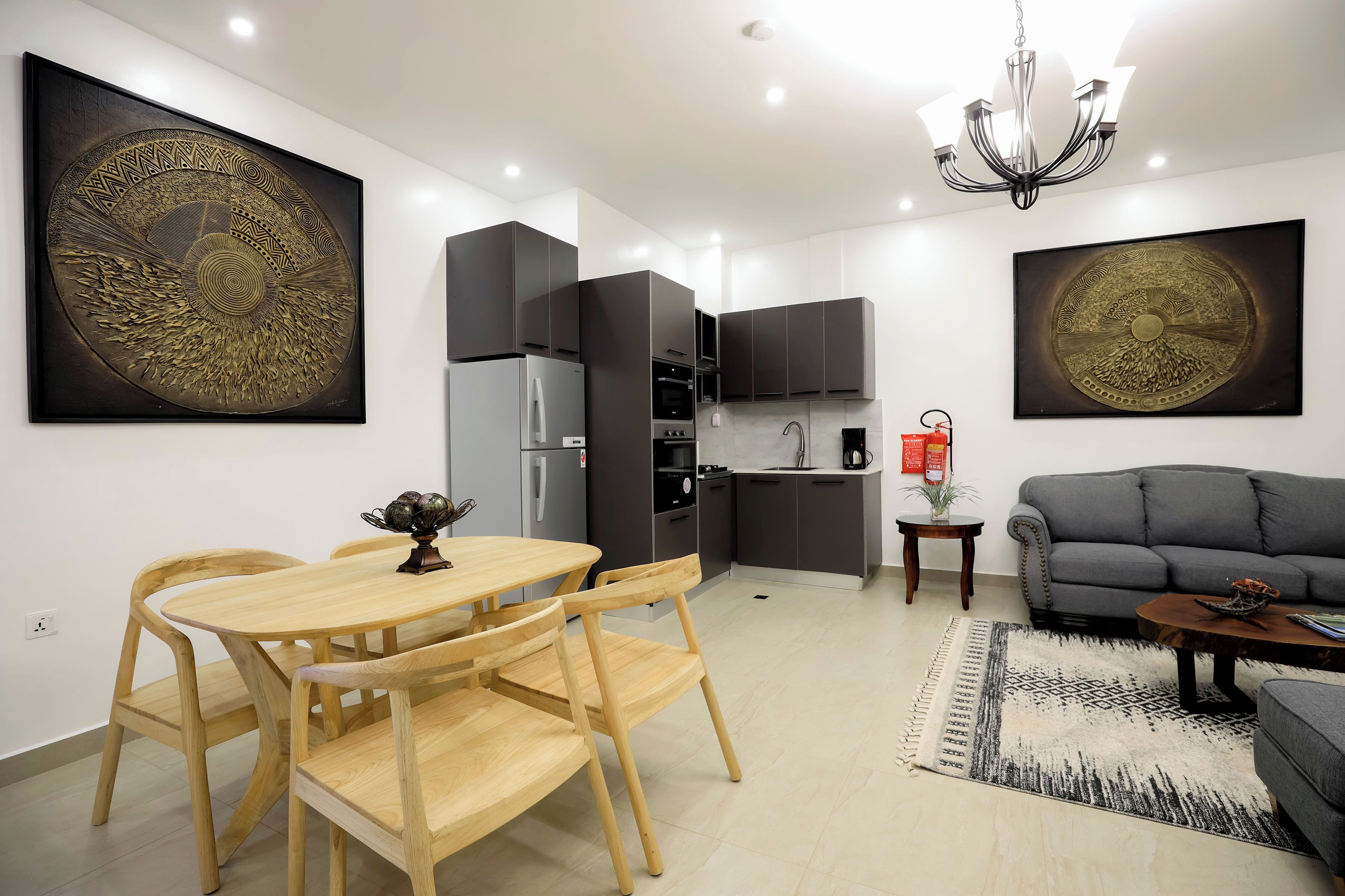 Una cocina moderna con armarios oscuros, un refrigerador y un comedor con sillas y una mesa de madera.