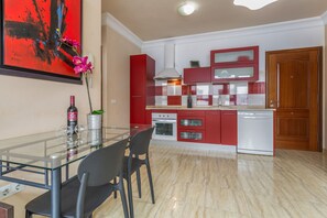 A modern kitchen with red cabinets, a glass dining table, and a large red and black painting on the wall. - Vacation 'Pto Rosario 4pax' with Wi-Fi (Puerto del Rosario)