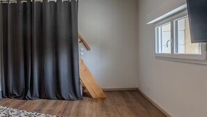 Une pièce avec un escalier en bois, un rideau noir, une fenêtre et un téléviseur à écran plat fixé au mur.